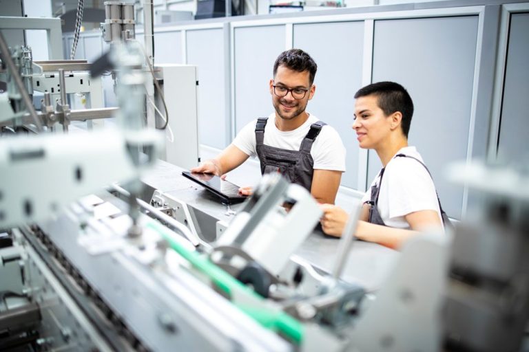 Zwei Personen in der Produktion diskutieren an einer Maschinensteuerung.